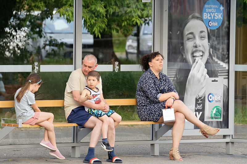 8 - A family and another adult sitting together on a bench at an urban bus stop